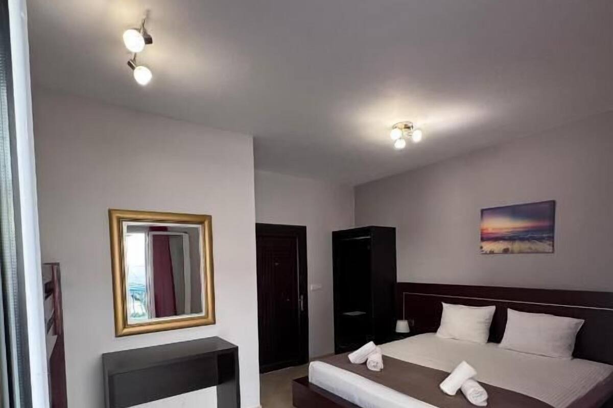 A hotel room with a large bed, a bedside table, a wardrobe, a mirror, and a painting on the wall.