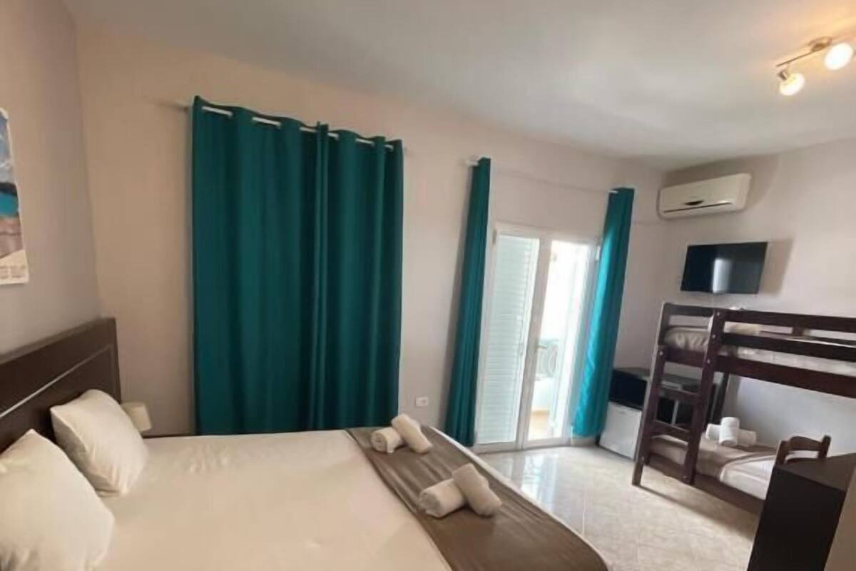 A hotel room with a bed, a desk, a TV, and a balcony with curtains.