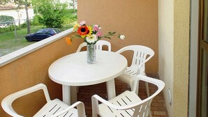 A small outdoor patio with a round table and four white plastic chairs. A vase with flowers is placed on the table. - Have a Nice Stay in our Well-equipped Flat With Balcony (Lignano Sabbiadoro)