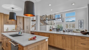 Cocina moderna con armarios de madera, una isla grande, iluminación colgante y vistas al exterior.