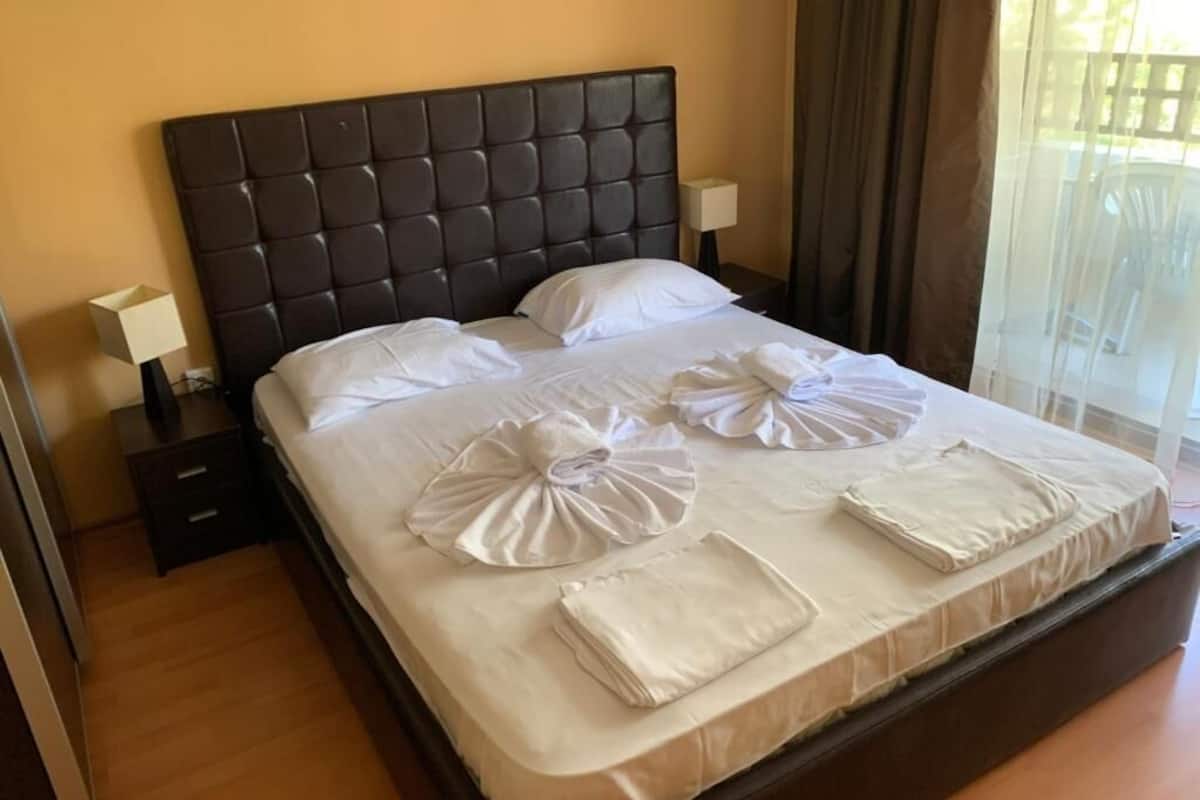 A neatly made bed with white linens and towels, a dark headboard, and a bedside table with a lamp.
