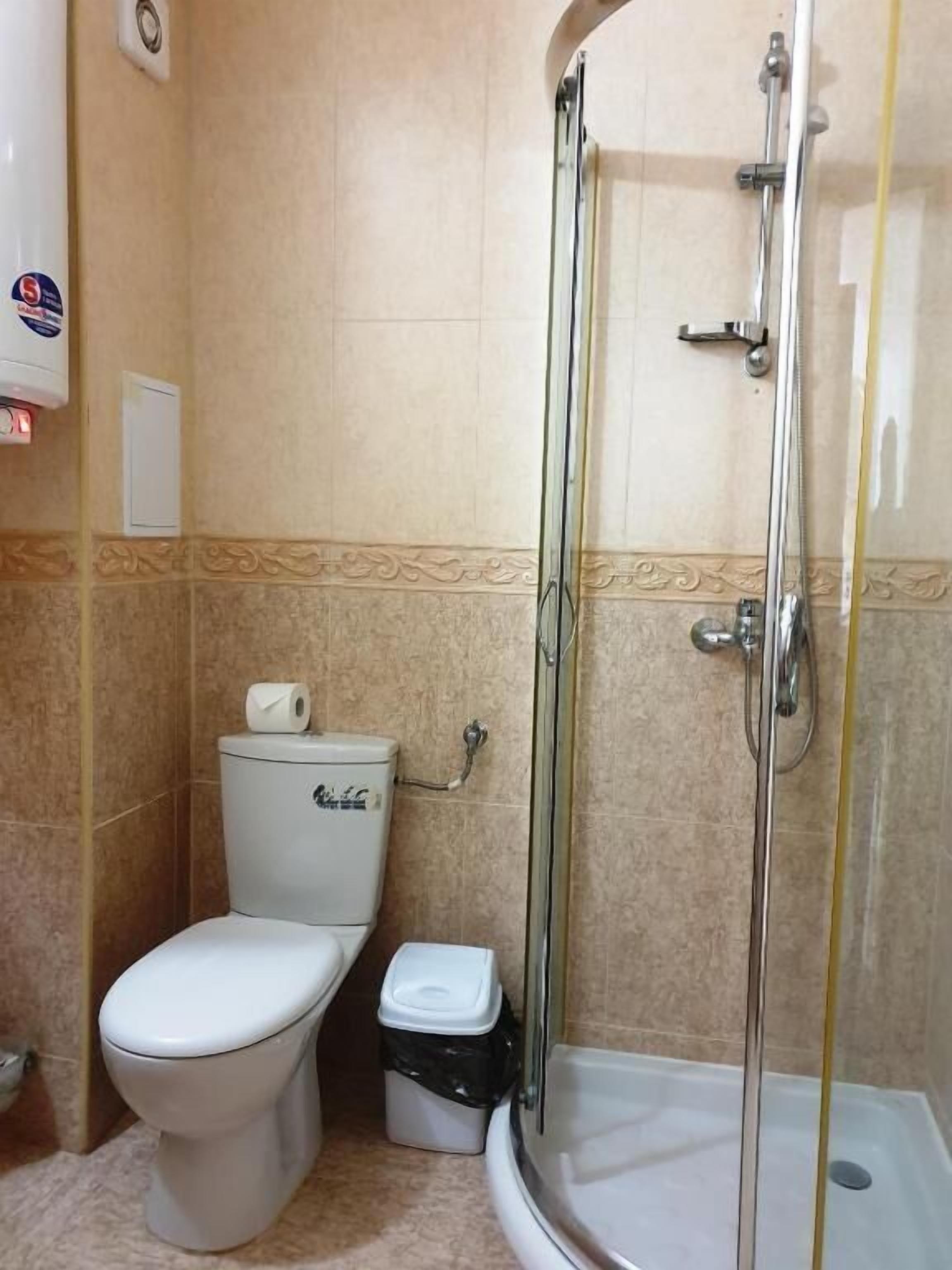 A bathroom with a toilet, a shower enclosure, and a trash bin.