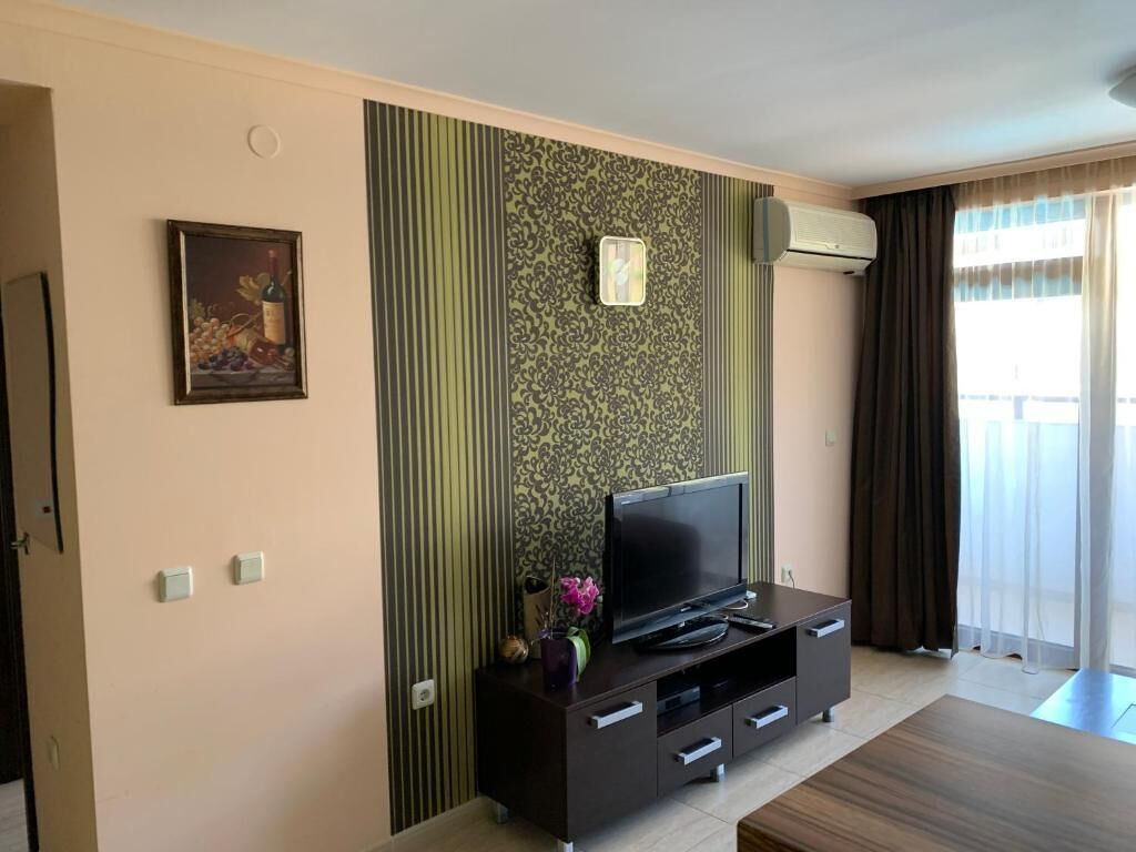 Un salon avec un téléviseur à écran plat posé sur un meuble de rangement en bois foncé, un tableau encadré accroché au mur et une fenêtre avec des rideaux.