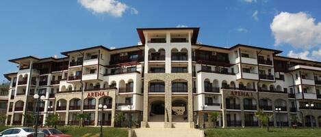 A multi-story hotel with a central entrance, balconies, and a clear sky.