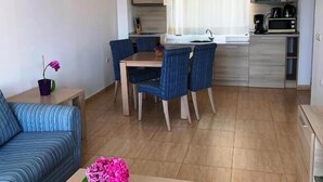 Een moderne woonkamer met een bank, een bijzettafeltje met bloemen, en een eethoek met stoelen en een tafel.
