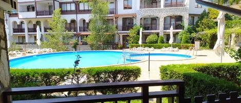 Ein Poolbereich mit einem klaren, blauen Pool, umgeben von einem gepflegten Garten und einem mehrstöckigen Gebäude mit Balkonen.