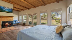 A bedroom with a large bed, a fireplace, and a view of the outdoors.