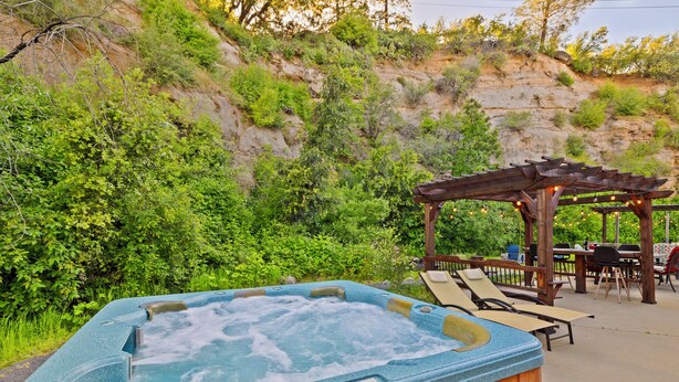 A hot tub with a control panel, surrounded by a wooden pergola and outdoor seating area with tables and chairs.