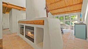 A spacious room with a fireplace, wooden beams, and large windows.