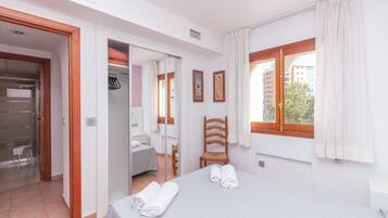 Un dormitorio con cama, una silla, ventana con cortinas, armario y un espejo.