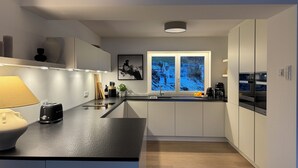 A modern kitchen with a central island, a built-in oven, and a window with a view of a snowy landscape. - Vacation home Allgäu: eat-in kitchen, fireplace, 4 bedrooms, 3 bathrooms, terrace & hot tub (Oberstdorf)