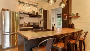 Una cocina moderna con un refrigerador de acero inoxidable, una isla de madera con taburetes de bar, iluminación colgante y una pared de ladrillo.