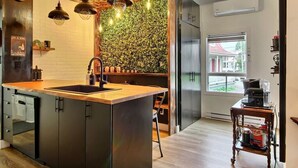 Una cocina moderna con una isla central, iluminación colgante, una pared de ladrillo y vistas al exterior.