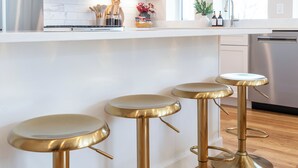 Une cuisine avec trois tabourets de bar de couleur dorée, un comptoir blanc et un lave-vaisselle en acier inoxydable.