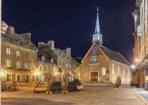 Un edificio histórico con un campanario destacado y un amplio ventanal circular, rodeado de calles adoquinadas y arquitectura tradicional.