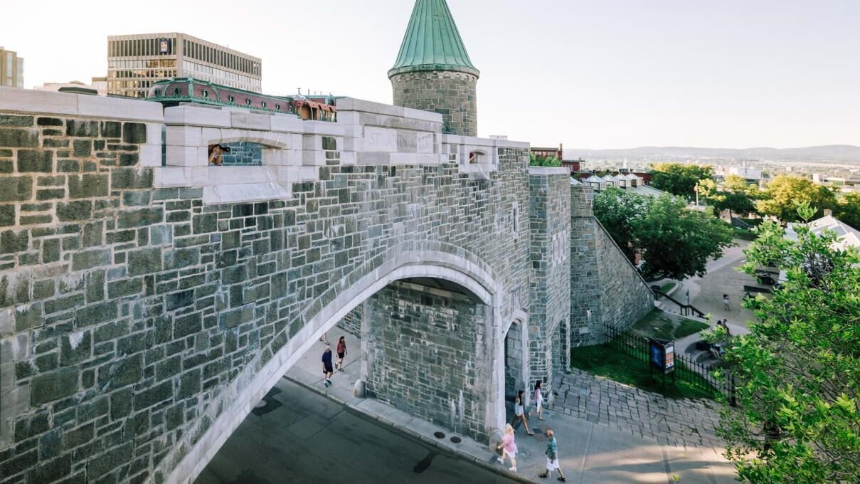 Un puente de piedra con un arco que da a un edificio histórico de techo verde.
