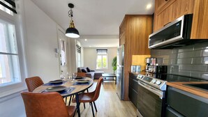 Et moderne køkken med indbygget ovn, mikroovn og kaffemaskine. Spiseområde med bord og stole.