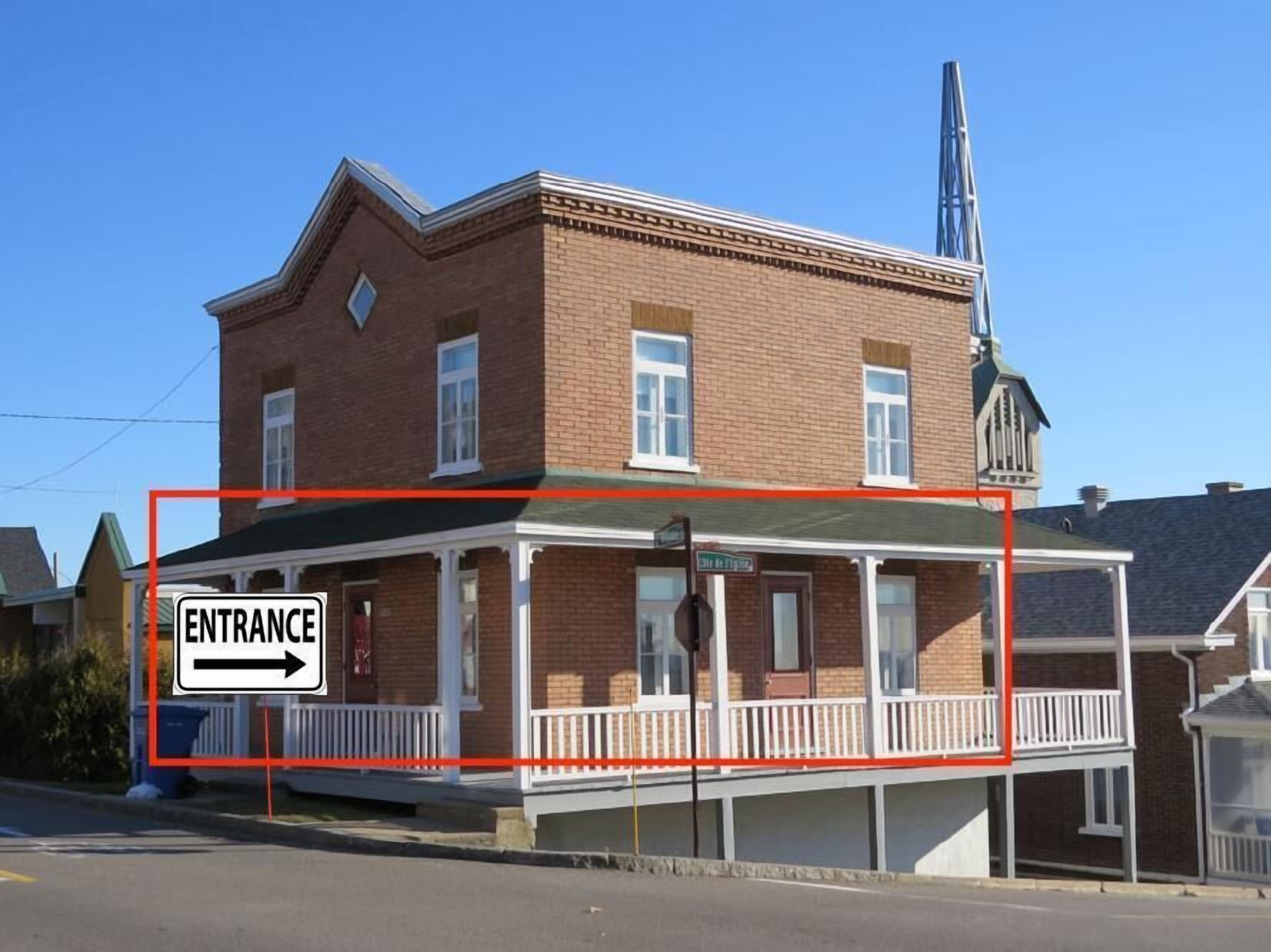 A two-story brick building with a covered entrance area, a visible fire hydrant, and a sign indicating the entrance direction.