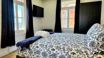 A bedroom with a bed, a TV mounted on the wall, and a window with curtains.