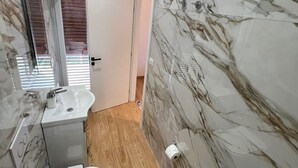 Un bagno con il water, un lavandino e uno specchio. Le pareti sono rivestite in marmo e il pavimento è in legno.