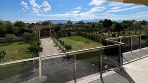 Un balcone con vista su un paesaggio verde, una zona pavimentata e un edificio in lontananza.