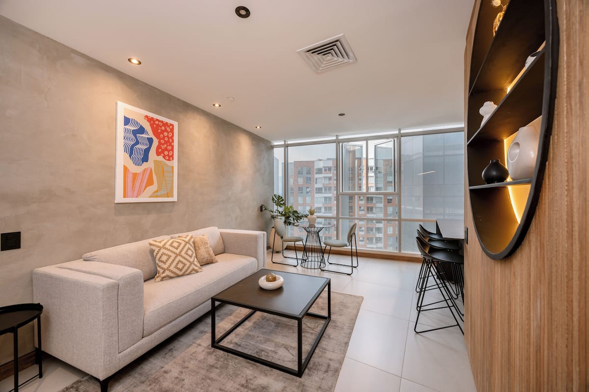 A modern living room with a sofa, coffee table, and a large window offering a city view.