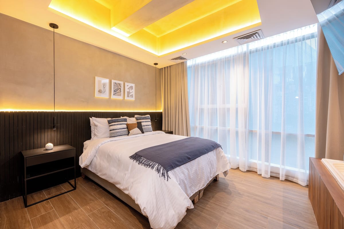 A modern bedroom with a large bed, bedside tables, and a view of the outdoors through sheer curtains.