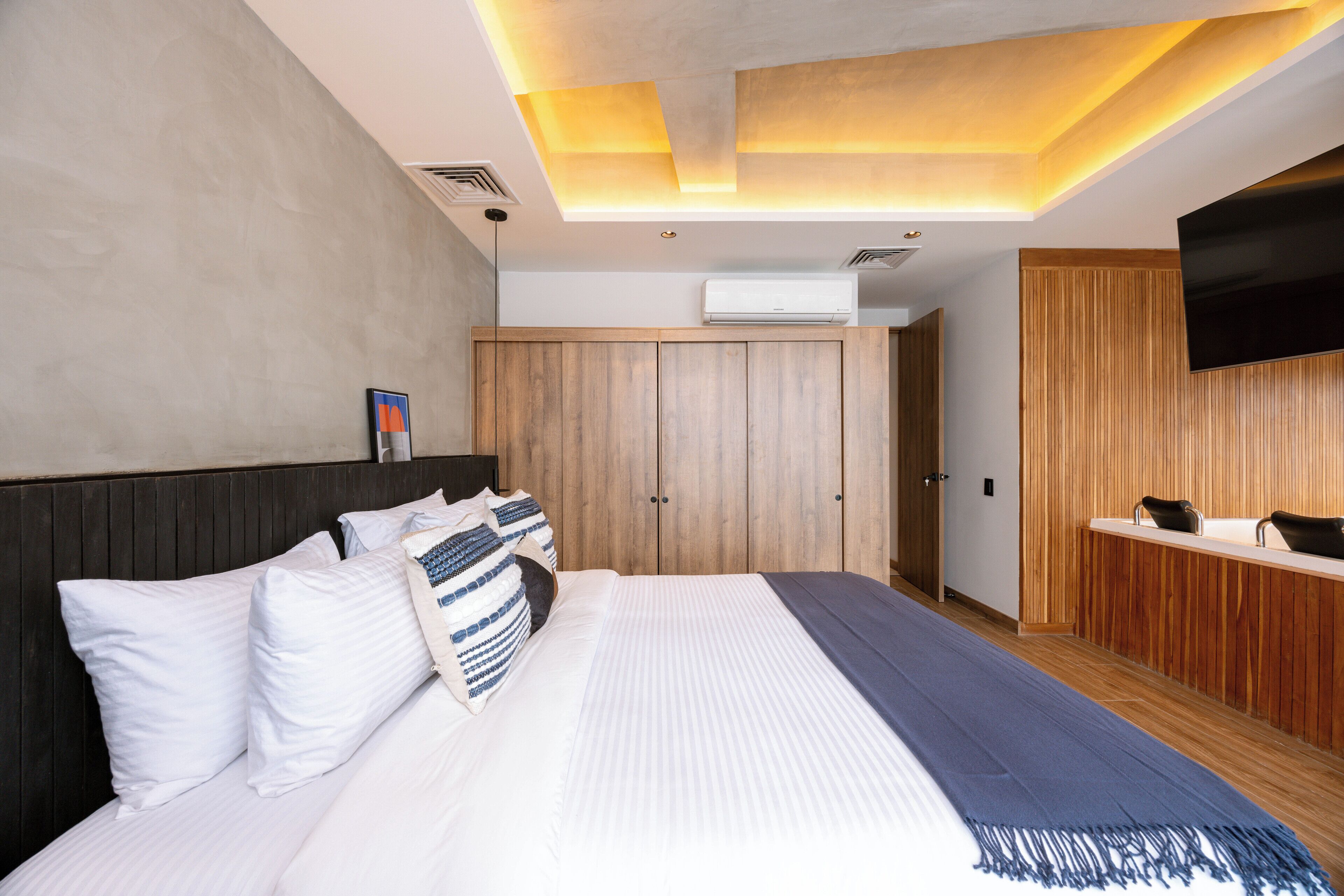 A modern hotel room with a large bed, wooden wardrobe, and a flat-screen TV mounted on the wall.