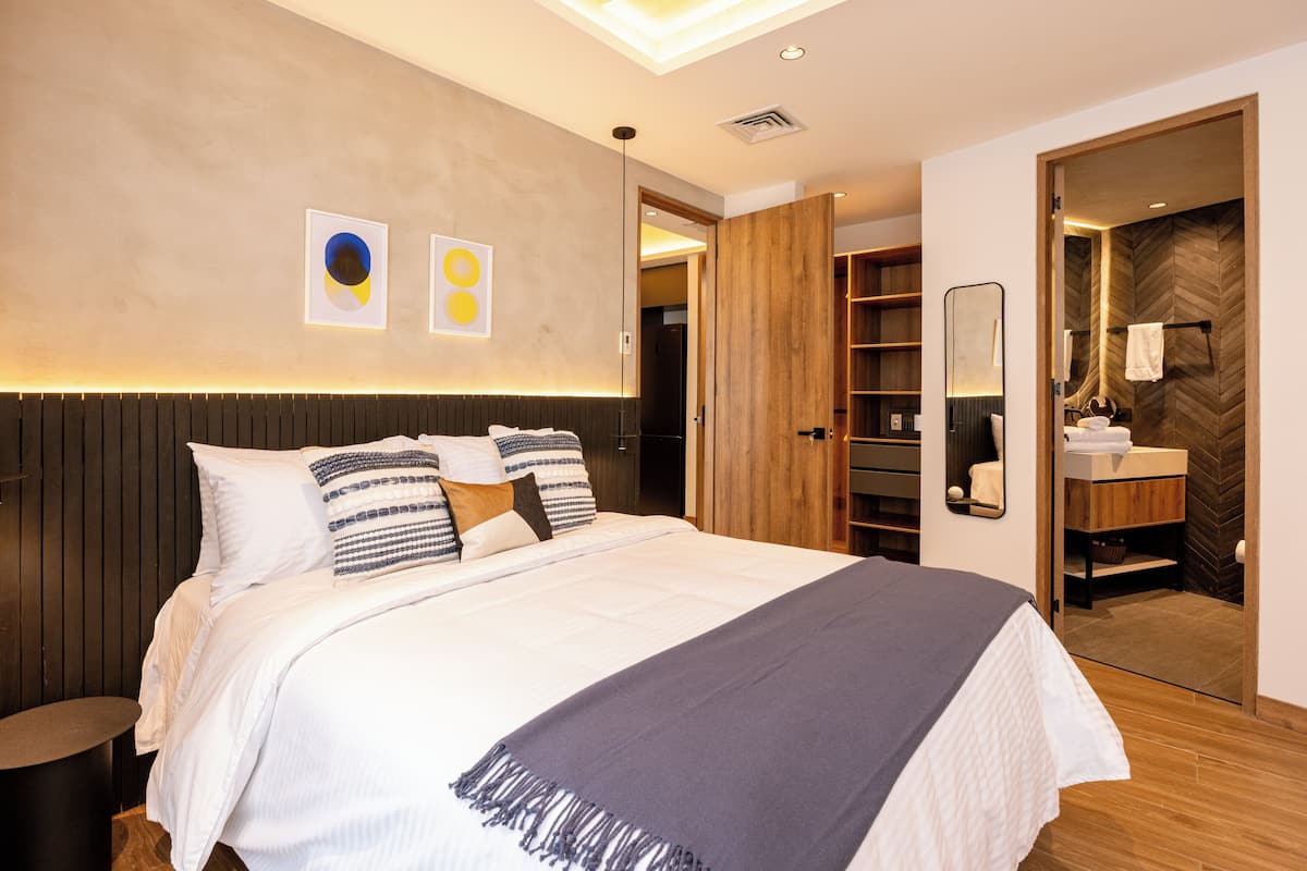 A modern bedroom with a large bed, bedside tables, a wardrobe, and a bathroom visible through an open door.