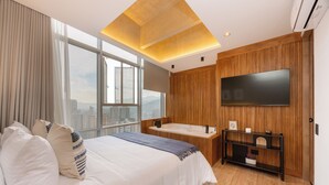 A modern bedroom with a large bed, a built-in bathtub, a TV mounted on the wall, and a city view through large windows. - Bio 26 Apartments  (Medellín)