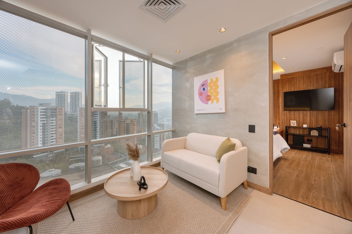 A modern living room with a large window, a white sofa, a red chair, and a round coffee table.