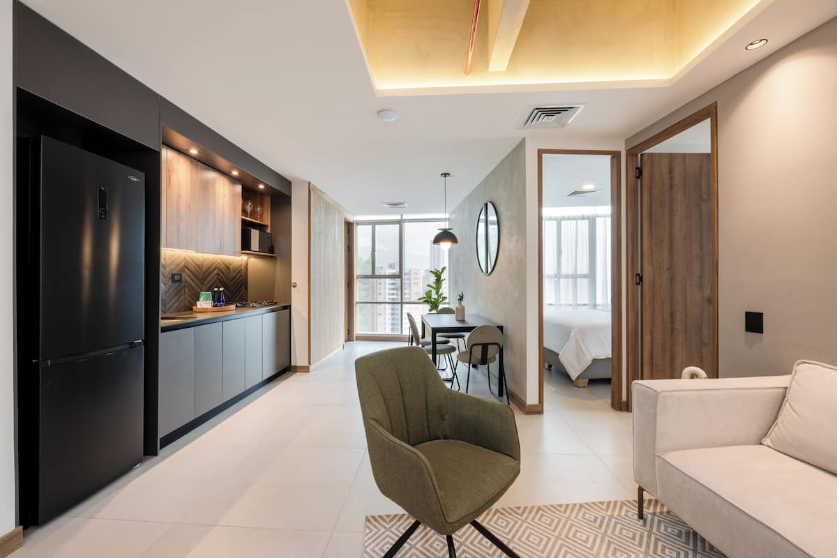 A modern kitchen with dark cabinetry, a dining area with a table and chairs, and a living area with a sofa.