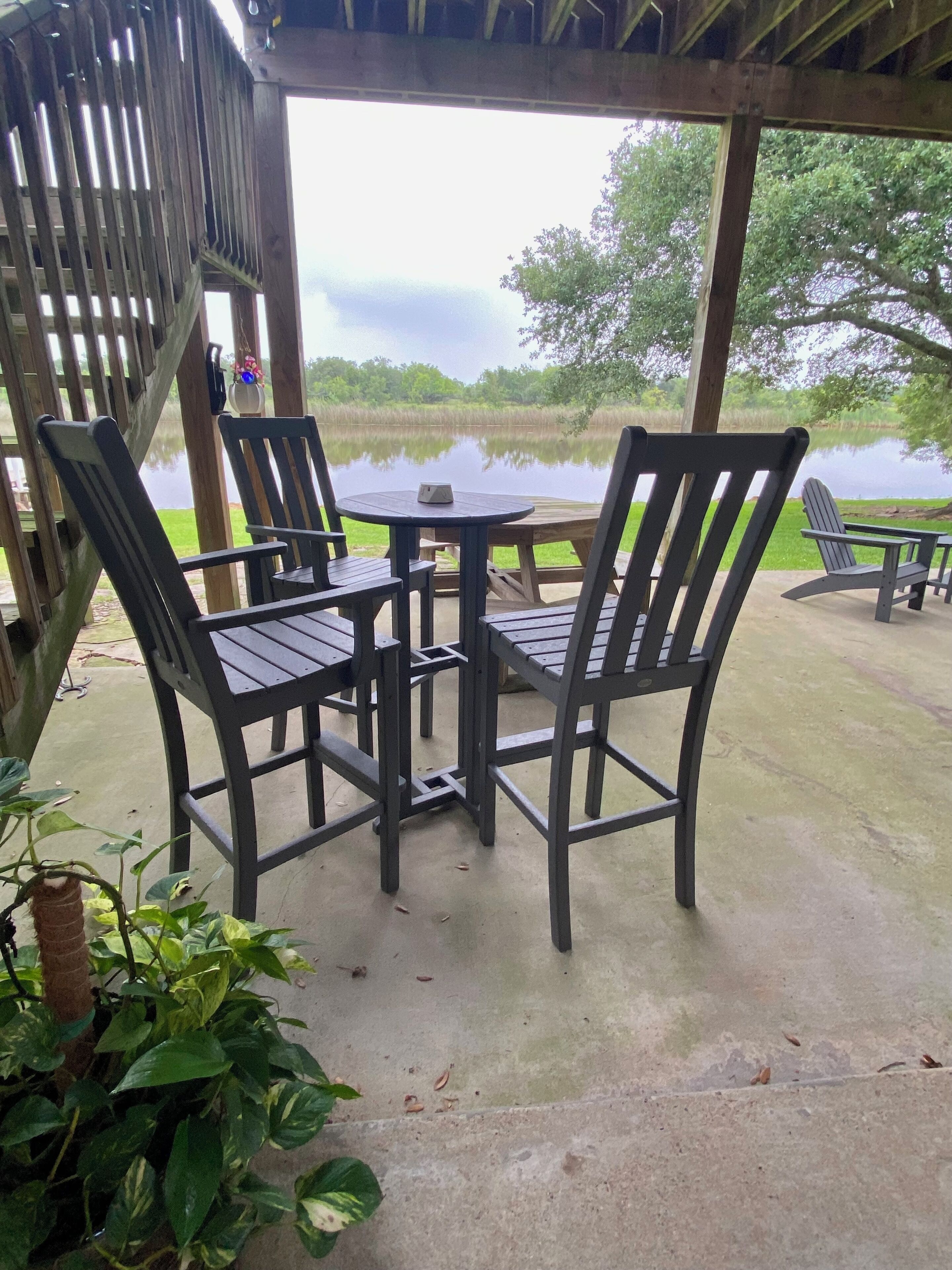 A covered outdoor seating area with a table and chairs, overlooking a body of water.