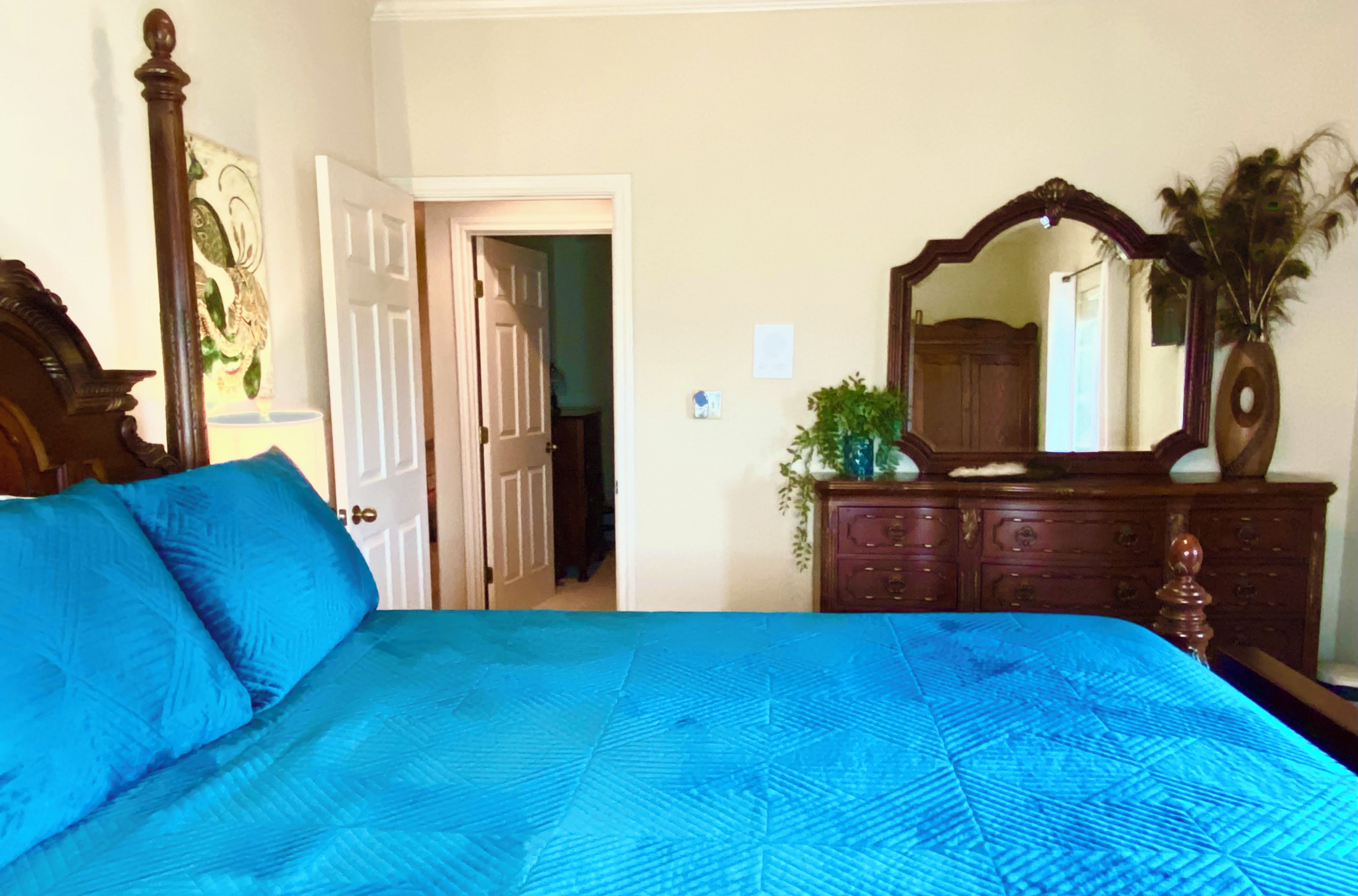 Une chambre à coucher avec un grand lit, une commode avec un miroir et une porte donnant sur une autre pièce.