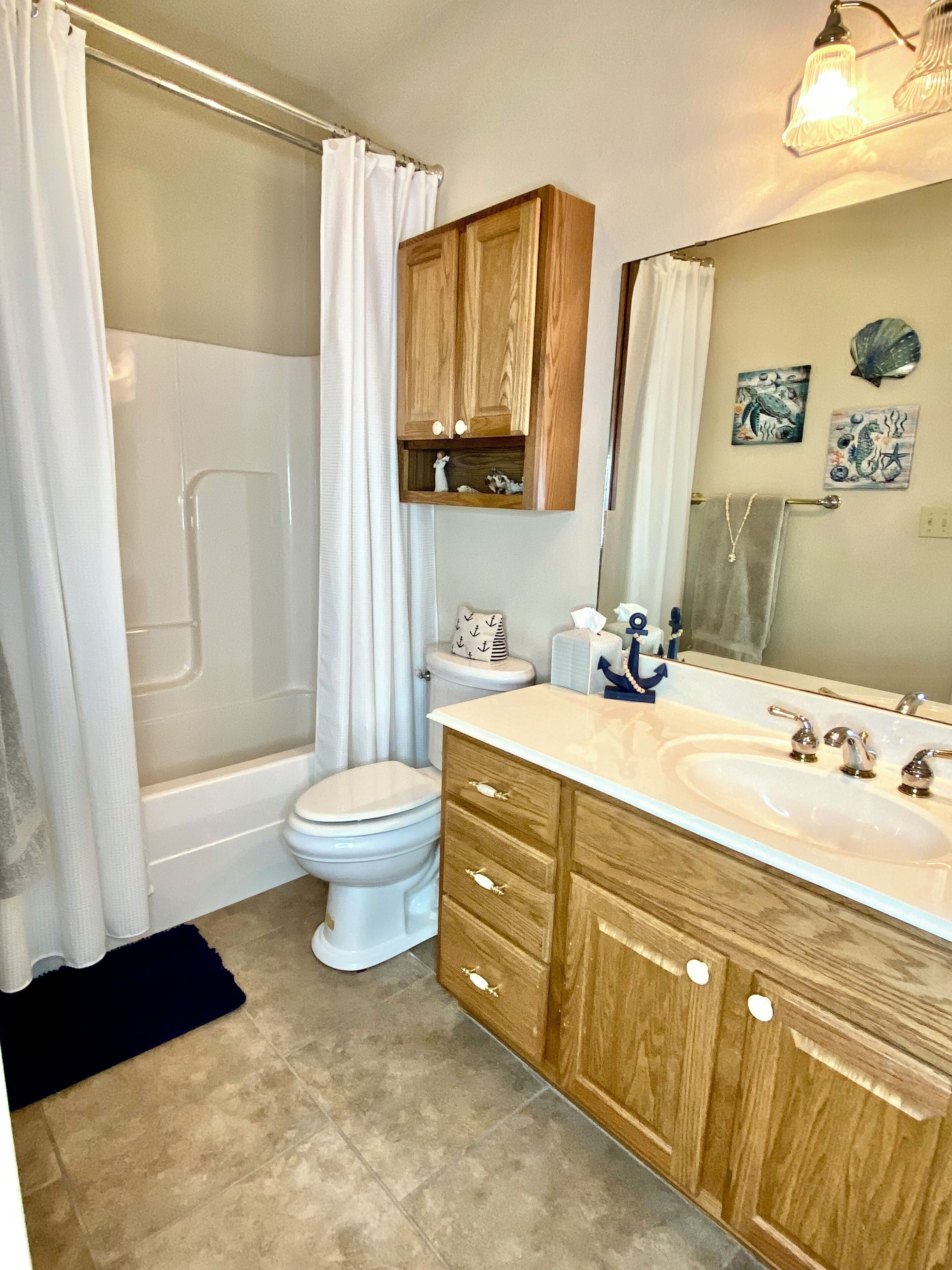 A bathroom with a shower, toilet, vanity with drawers, and a large mirror.