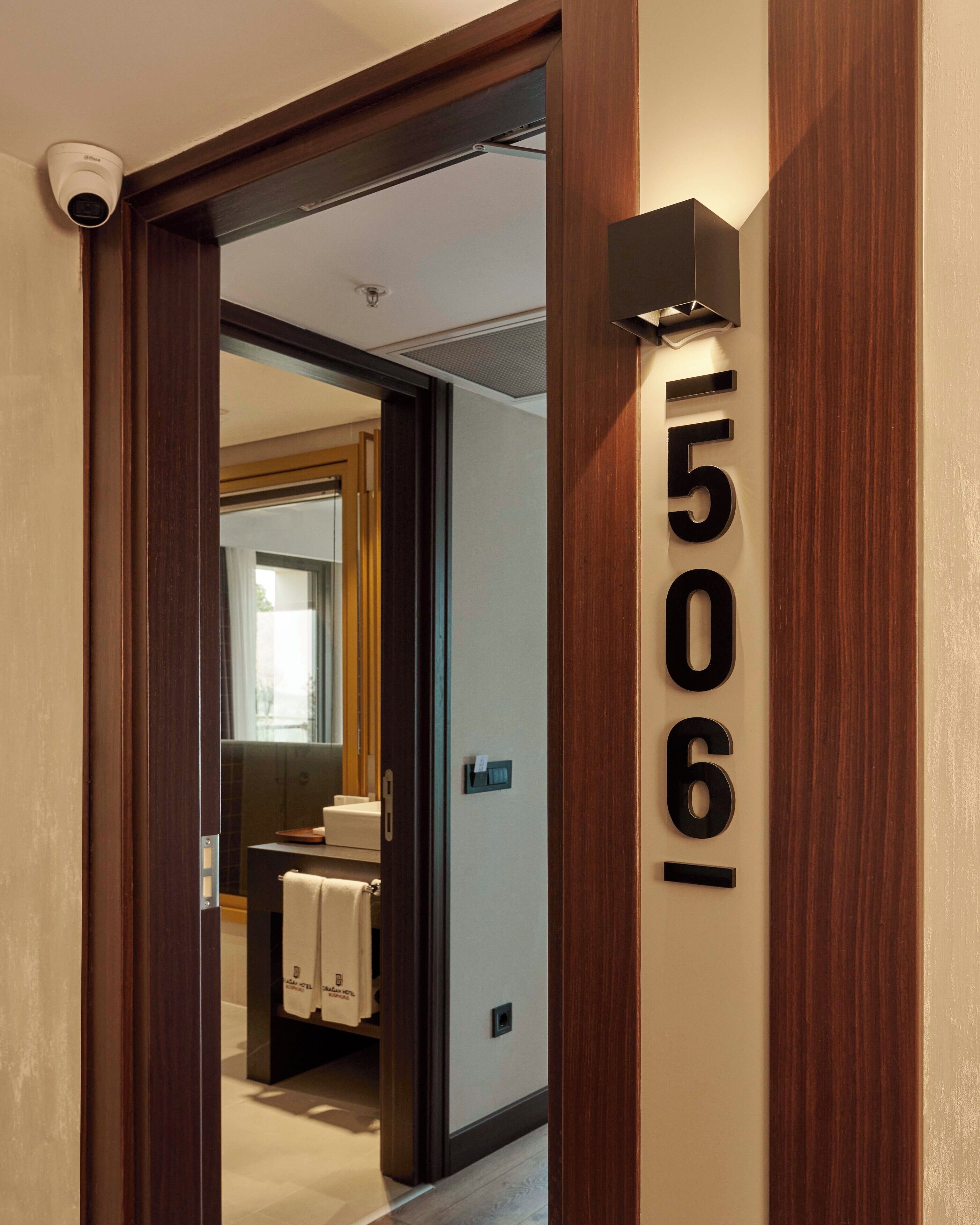A hotel room with a wooden door frame, a number sign, and a glimpse of a bathroom with a towel rack.