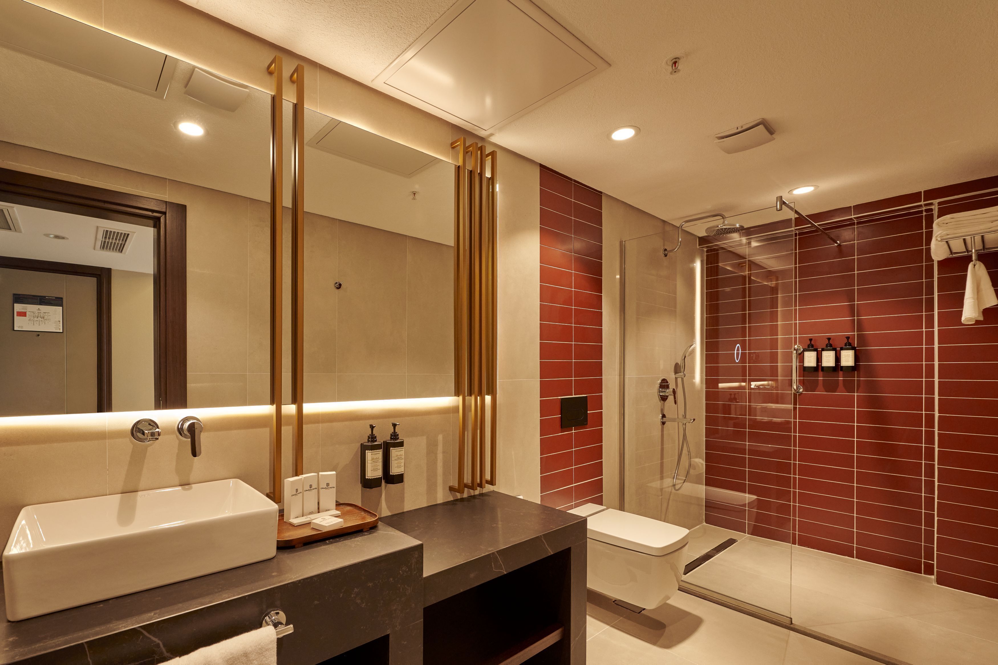 A modern bathroom with a large mirror, a rectangular sink, a toilet, and a glass-enclosed shower area.