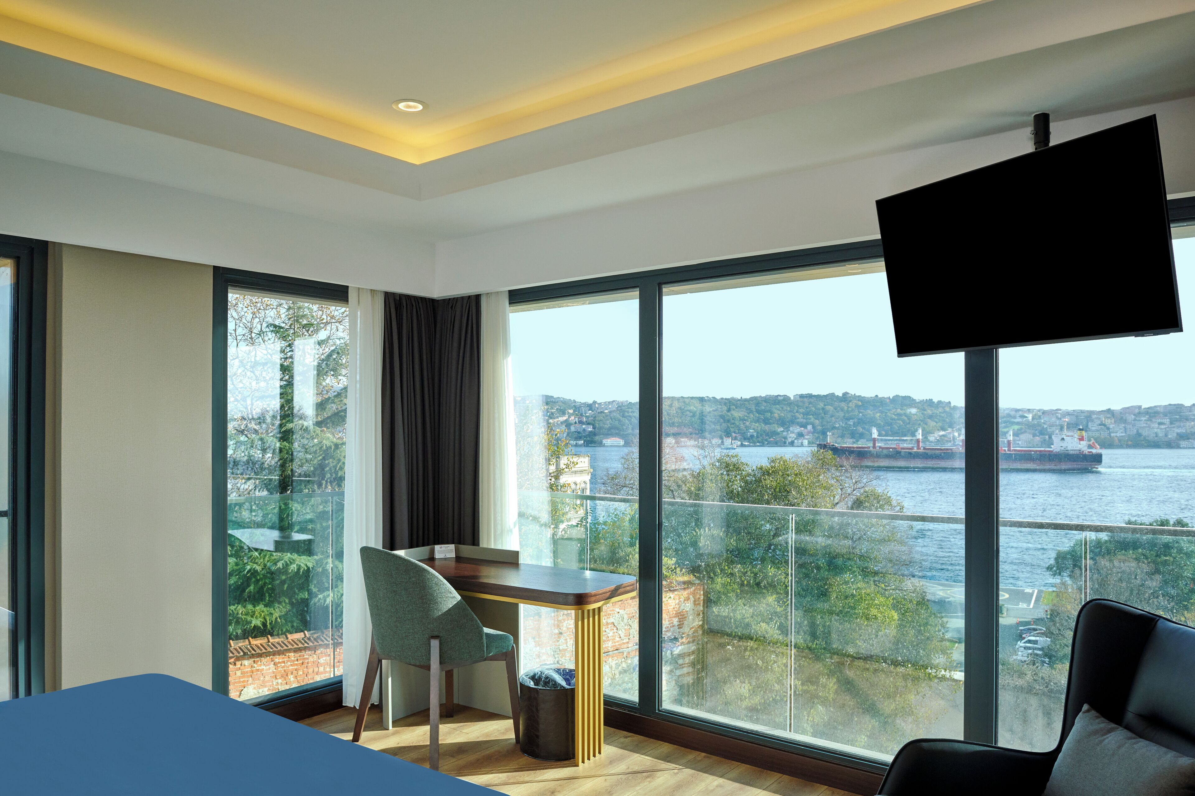Habitación de hotel moderna con un amplio ventanal que ofrece vistas a un río y al paisaje urbano.