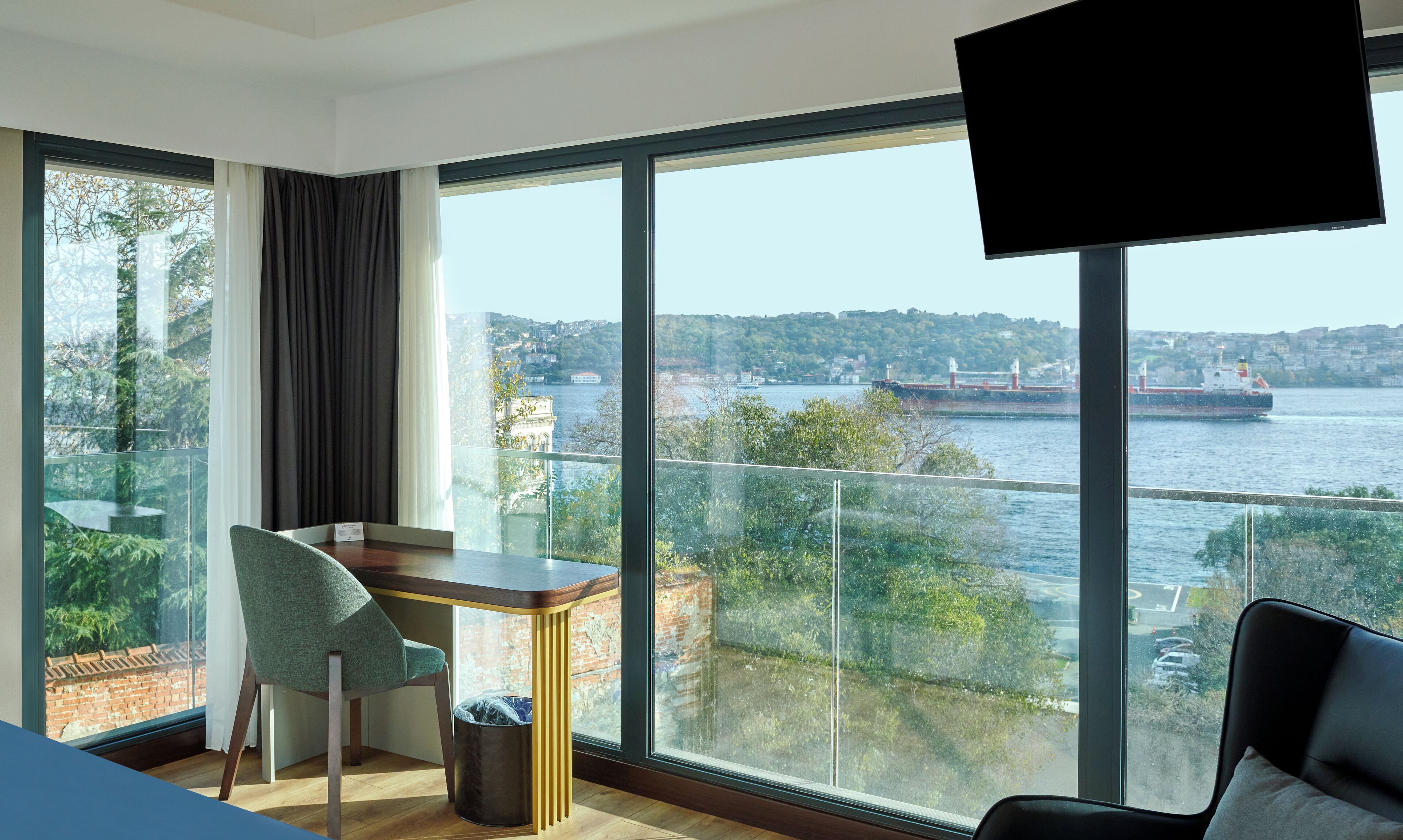 Habitación de hotel moderna con un ventanal que ofrece vistas a un río y al paisaje urbano.