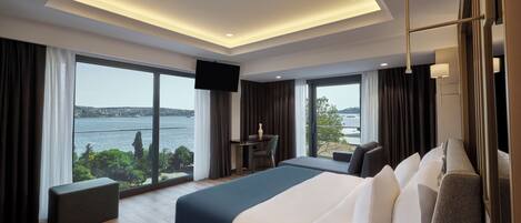 A modern hotel room with a large bed, a desk, and a view of a body of water.