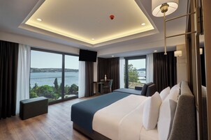 A modern hotel room with a large bed, a desk, and a view of a body of water.