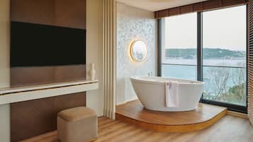 A modern bathroom with a freestanding bathtub, a large mirror, and a television mounted on the wall.