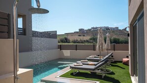 A modern outdoor pool area with a showerhead, lounge chairs, and a view of buildings in the background.