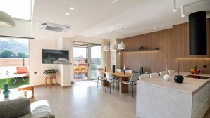A modern kitchen with a central island, a dining area with a table and chairs, and a living area with a sofa and a TV.