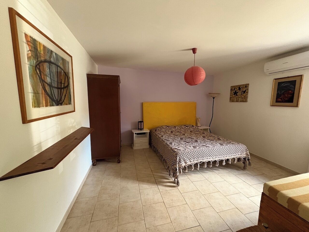 Une chambre à coucher comprenant un lit, une table de chevet, une armoire et une lampe suspendue rouge.