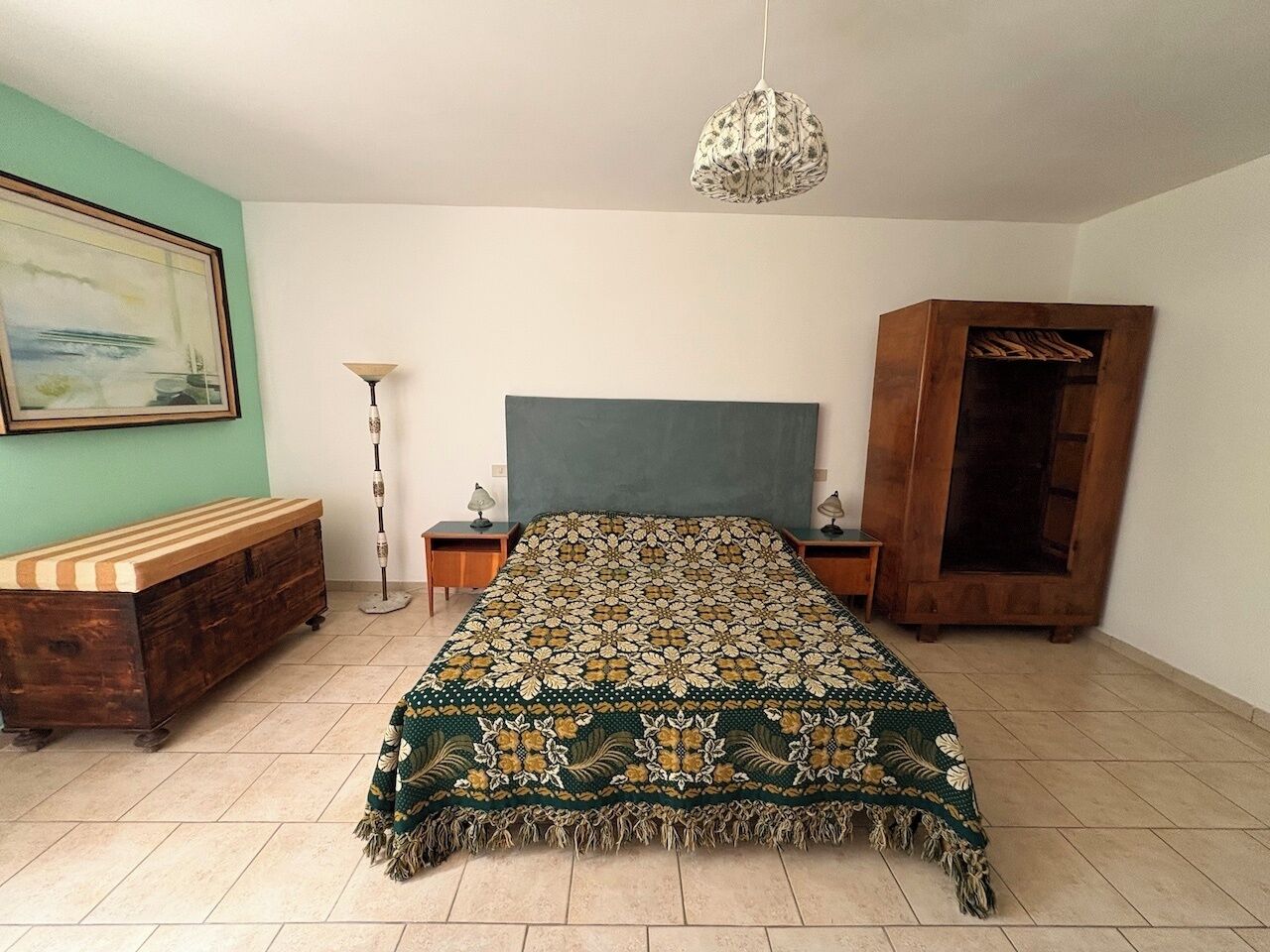 Una camera da letto con un letto, una testiera in legno, comodini, una lampada da terra e un armadio.