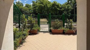 Een gebogen toegang tot een binnentuin met betegelde vloer, een groene poort en plantenpotten.