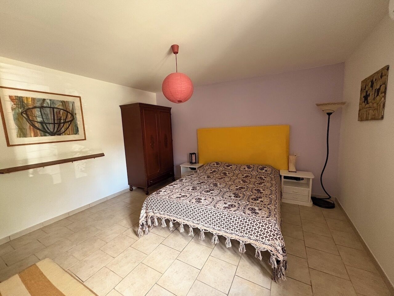 Ein Schlafzimmer mit einem Bett, einem Nachttisch, einer Lampe, einem Kleiderschrank und einem Bild an der Wand.