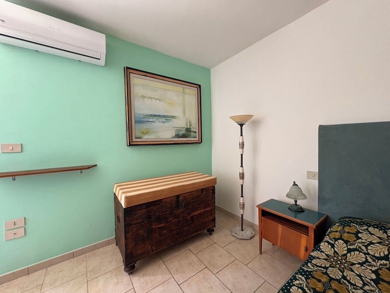 A room with a bed, a dresser, a lamp, and a painting on the wall.