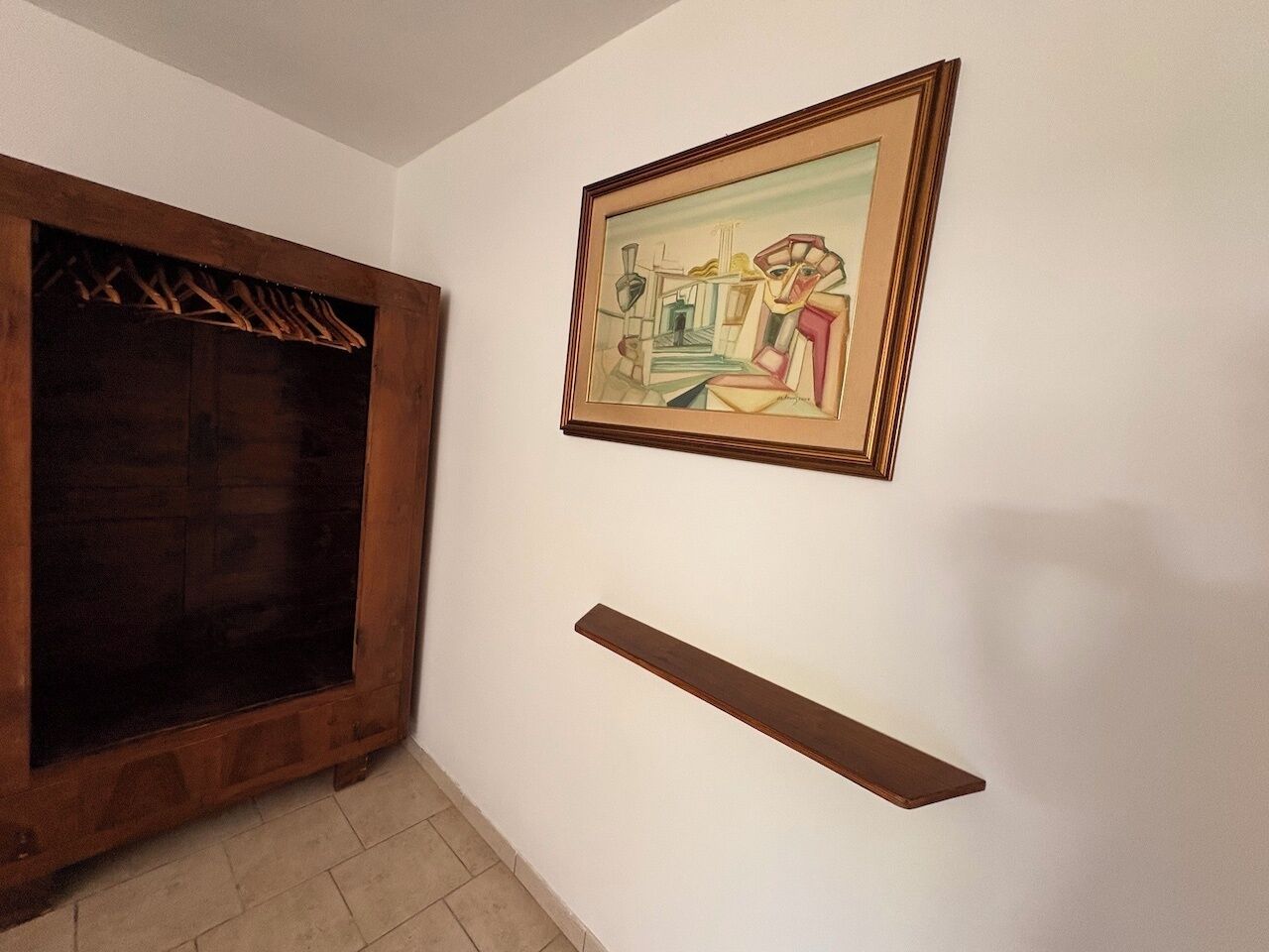 Une pièce avec une armoire en bois, un tableau abstrait encadré et une étagère murale.